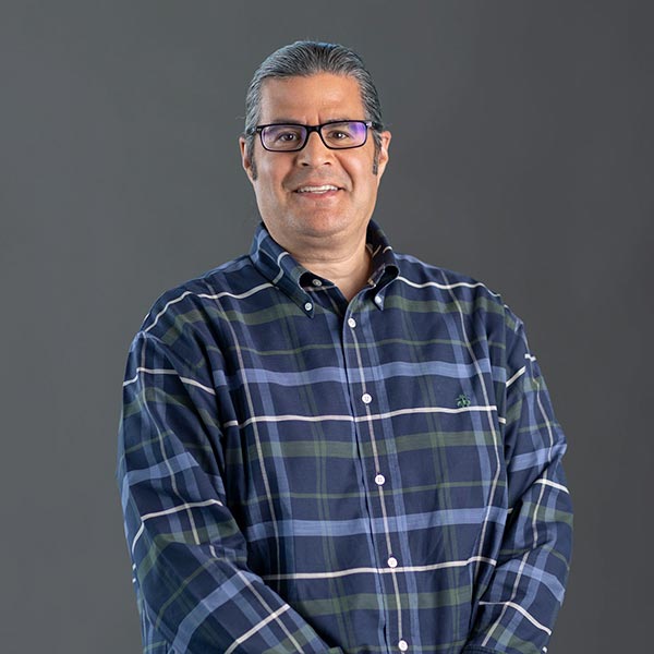 Portrait of a smiling man Marko Leal, VP of HR, with slicked back hair and glasses wearing a blue plaid shirt and smiling.