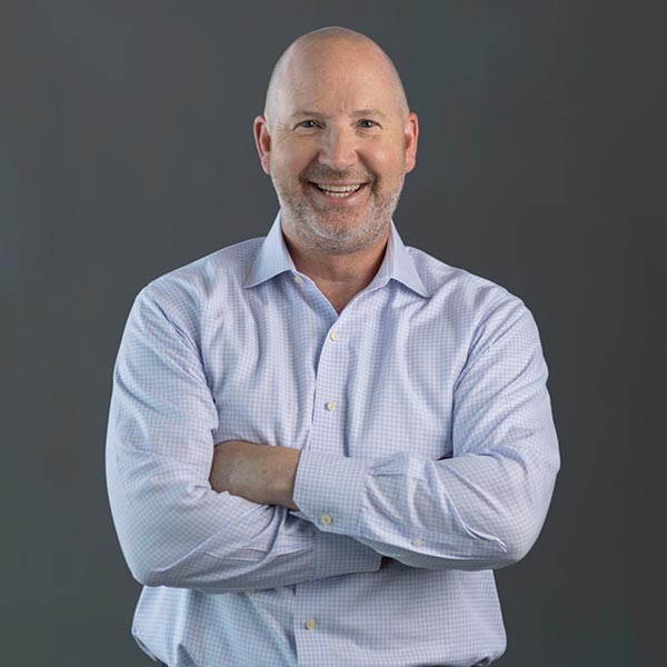 Portrait of a smiling man Mike Grindstaff, VP Sales, smiling for the camera with his arms crossed over his chest and wearing a blue shirt.