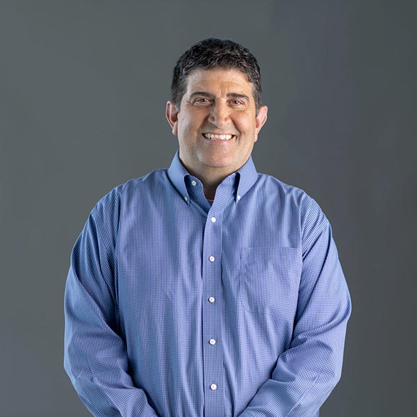 Portrait of a smiling dark-haired man Rob Miller, VP Supply Chain, wearing a blue shirt and smiling for the camera.