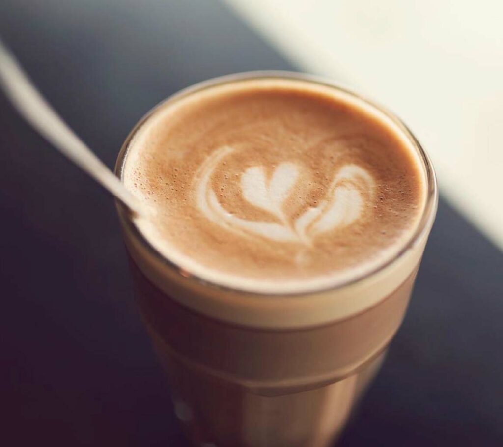 Chocolatey beverage in a clear glass with white heart design in top of froth. 