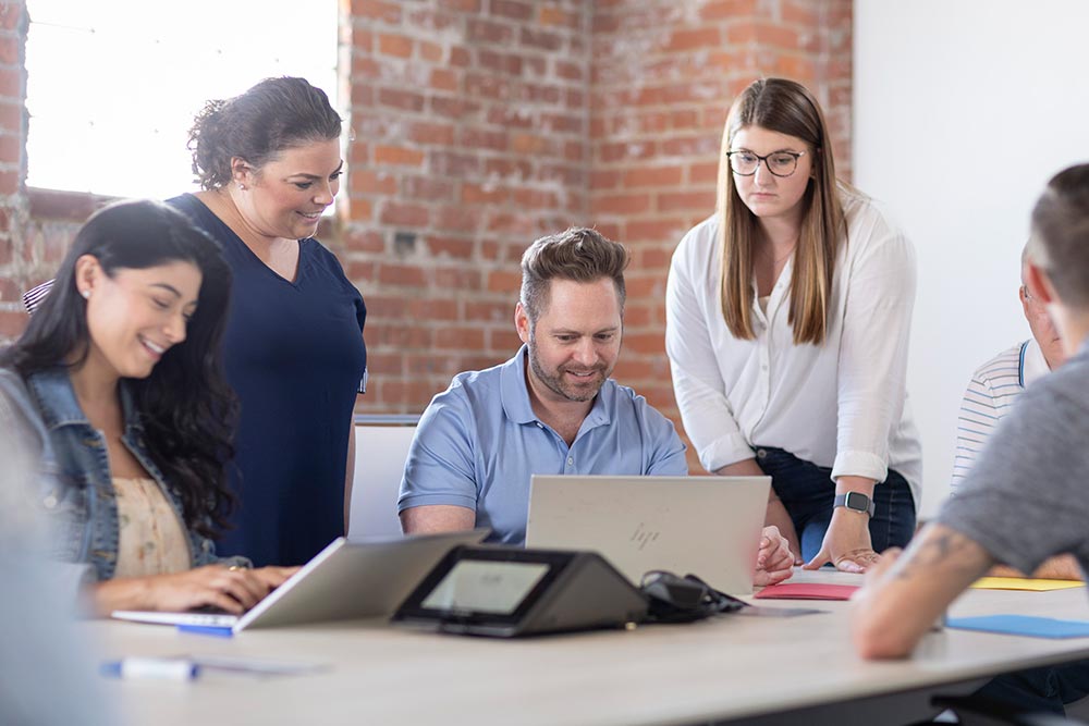 Four colleagues, two standing and two sitting, collaborate on a project.