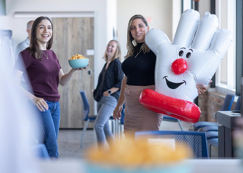 Employees in a break room sharing a laugh while one woman holds a Hamburger Helper mascot glove.