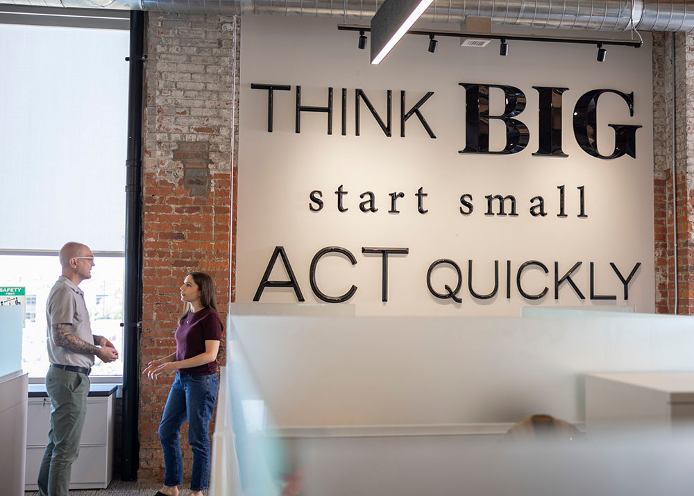 Two Eagle Foods employees talking next to a wall that says "Think BIG, start small, act quickly"